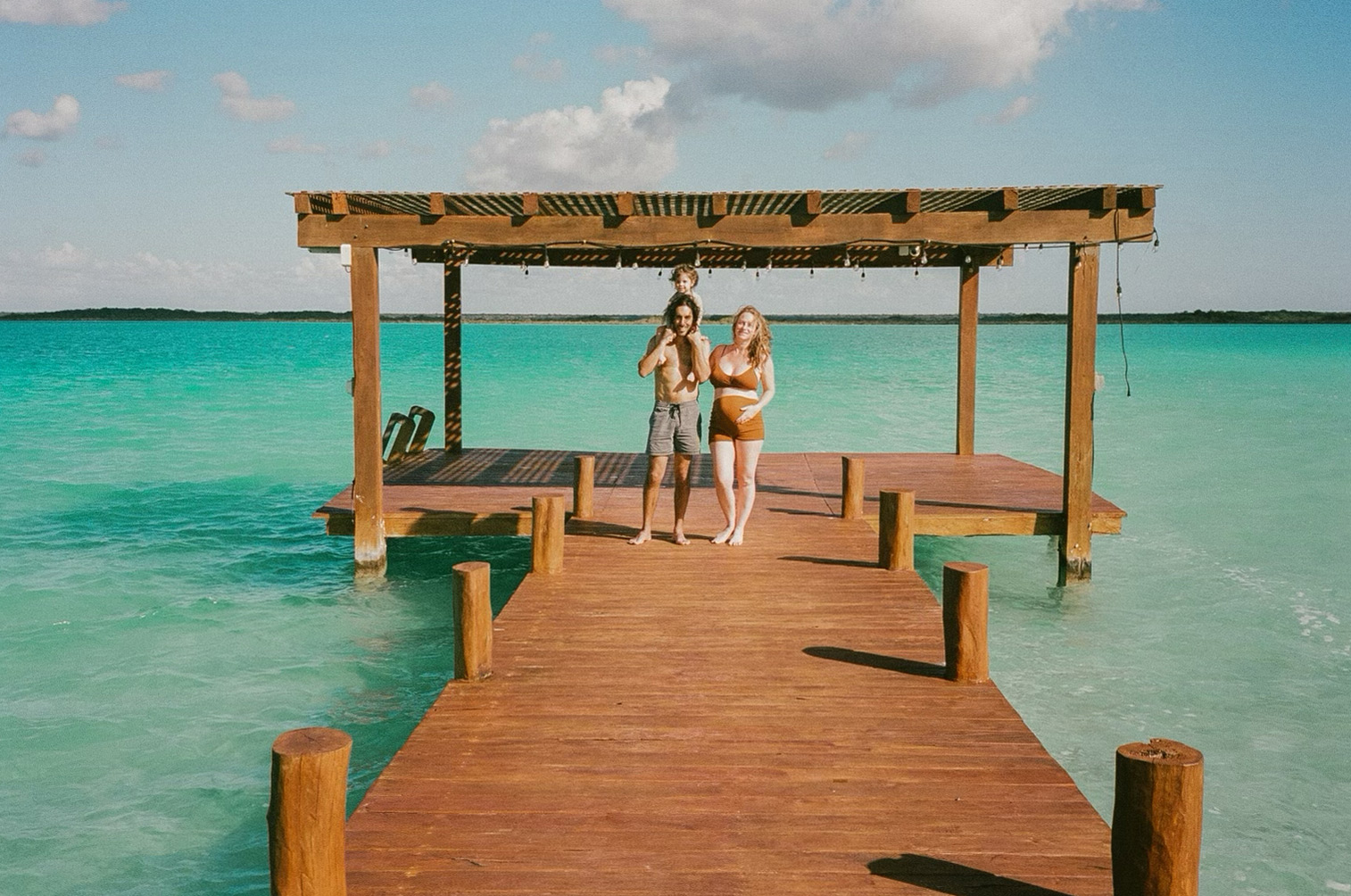 A family of three with a 6 month pregnant mother on a dock in Bacalar, Mexico.